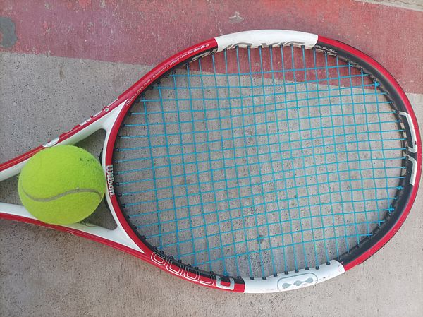 A tennis racket and a tennis ball are positioned on a concrete surface.