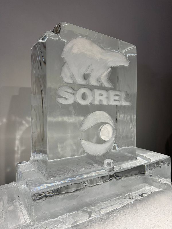 A street fashion scene from Fashion Week featuring a stylish woman wearing a floral blouse and denim shorts, holding a pink phone and a white bag, with a city background and a man walking by.