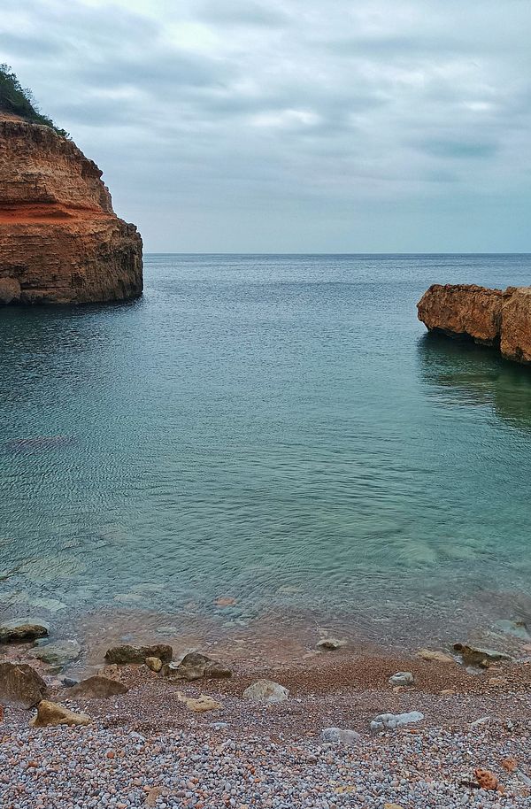 A serene coastal scene featuring calm waters and rocky cliffs under a cloudy sky.