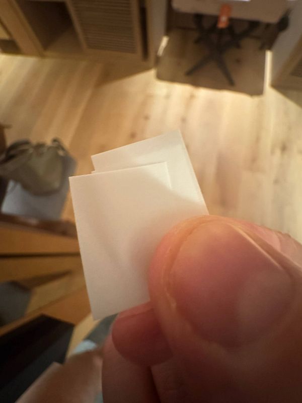 A person holds a small piece of eco-friendly toothpaste paper between their fingers.