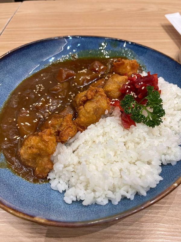 A plate of fried chicken with curry sauce and rice garnished with herbs.