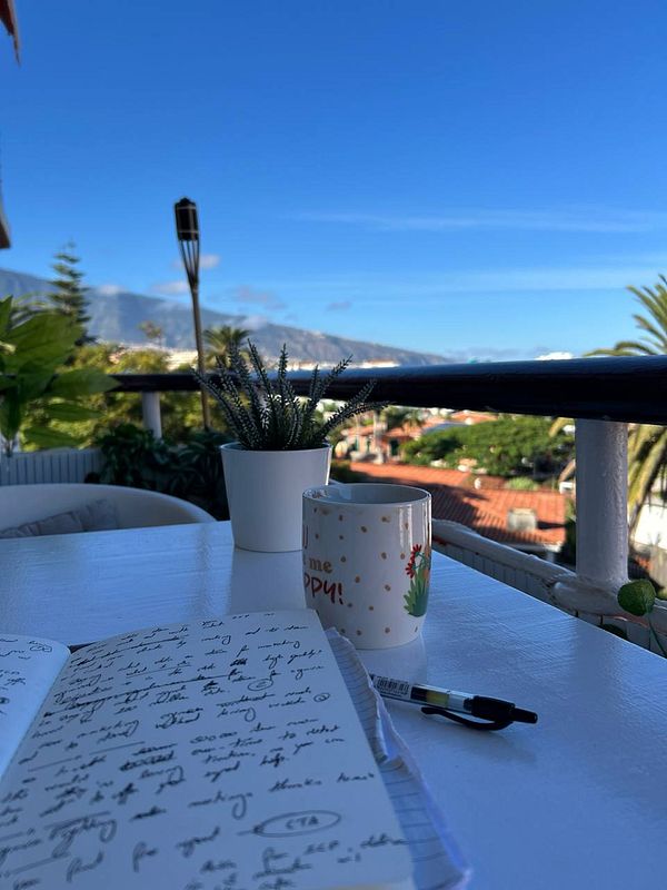 A serene outdoor workspace featuring a notebook, a coffee mug, and a view of a sunny landscape.