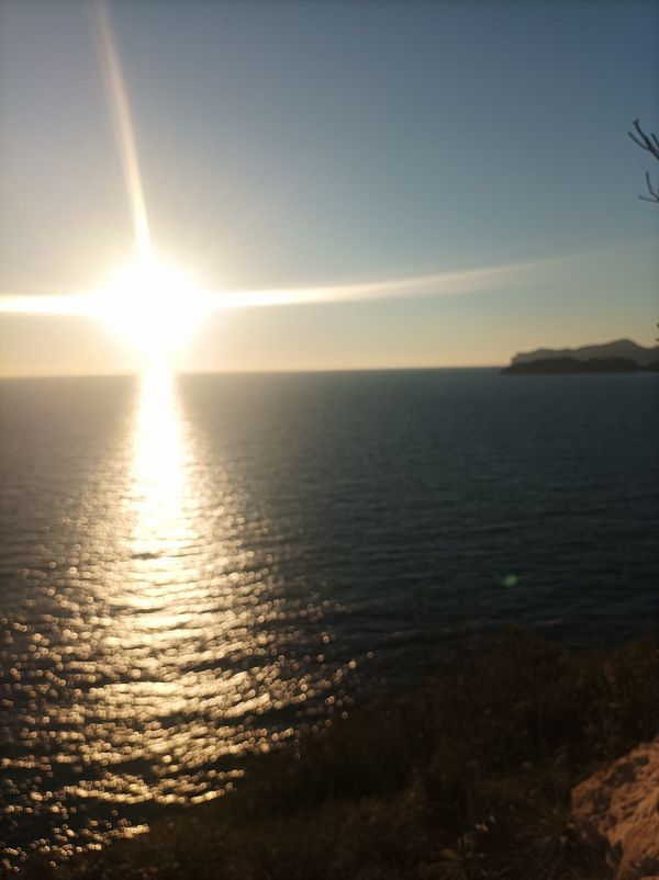 A stunning sunset over the ocean with shimmering water and a distant coastline.