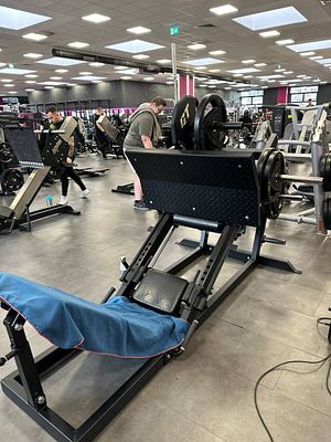 A gym scene featuring a leg press machine and several individuals working out.