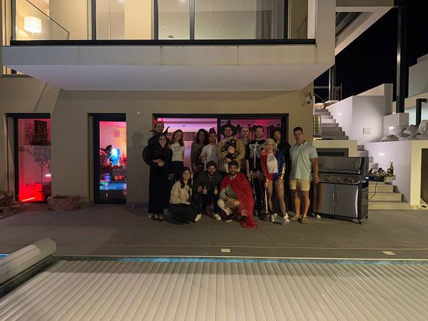 A group of friends dressed in Halloween costumes gathers for a BBQ party at a modern house.