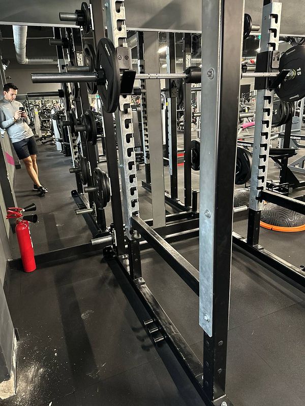 A gym interior featuring weightlifting equipment and a person using a smartphone.