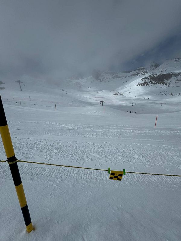 A snowy ski slope under cloudy skies with ski lifts in the background.