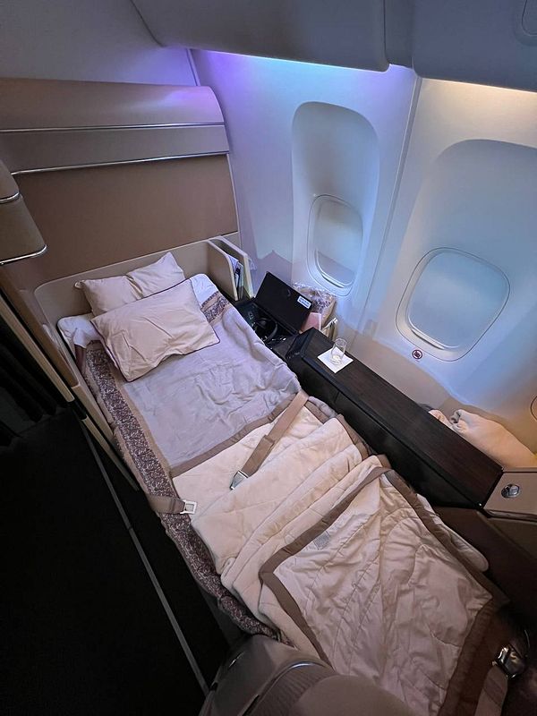 The image depicts a luxurious airplane cabin featuring a fully flat bed setup.
