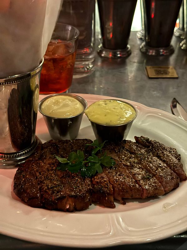 Grilled steak served on a white plate with sides of lettuce and sauce.