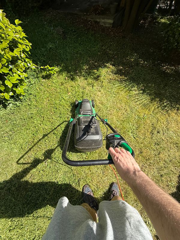 A person is preparing to mow the lawn with an electric lawn mower.
