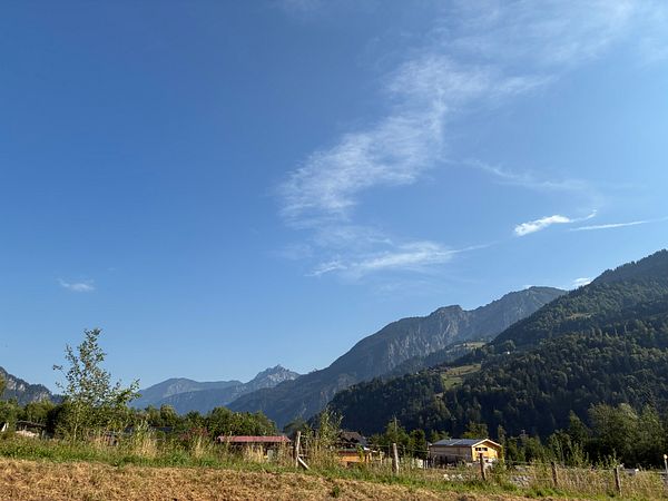 Sunlit mountainous landscape under a clear blue sky with a walking path and people walking.