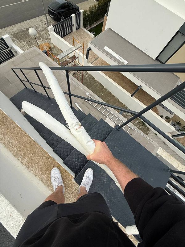 A person is holding large, wrapped items while standing on a staircase leading down from a rooftop.