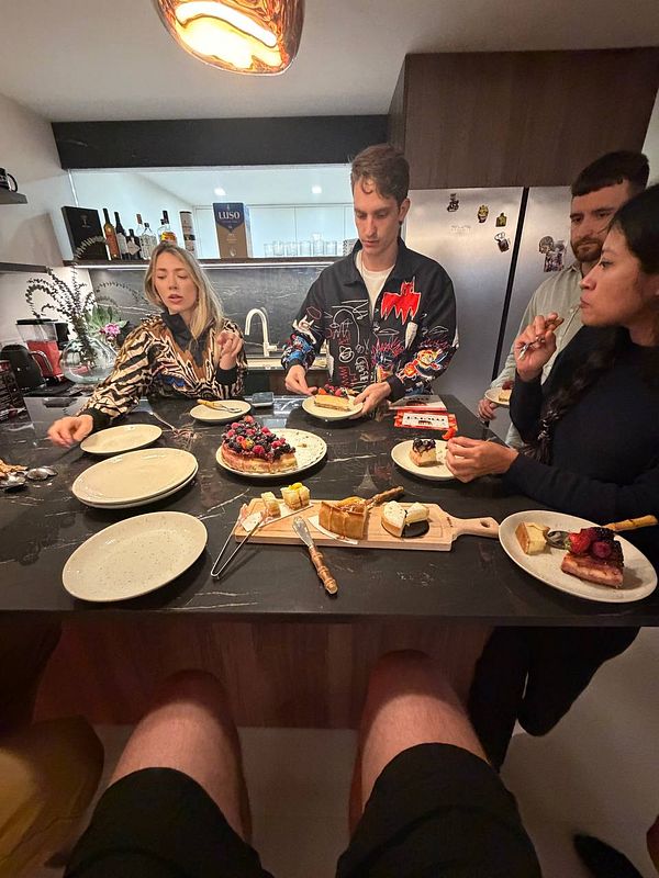 Four people sitting around a kitchen island enjoying desserts, with a variety of sweet treats on plates and a wooden board in the center.