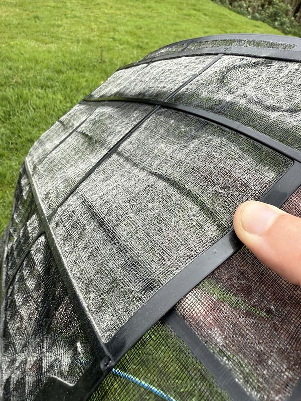 A close-up view of a dirty heat pump filter being pointed at by a finger.