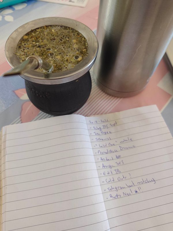 Portrait of a woman holding a mate cup with yerba mate leaves and a metal straw, smiling and seated indoors.