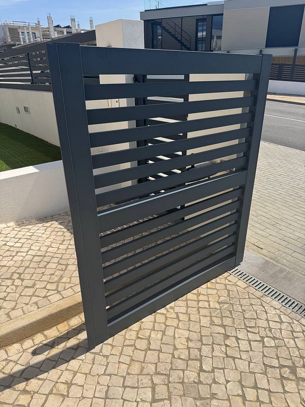 A damaged electric gate is leaning against a wall, unable to move due to its position.