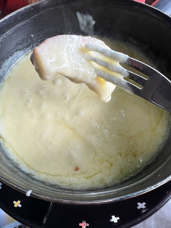 A fork holding a piece of bread is dipped into a bubbling pot of cheese fondue.