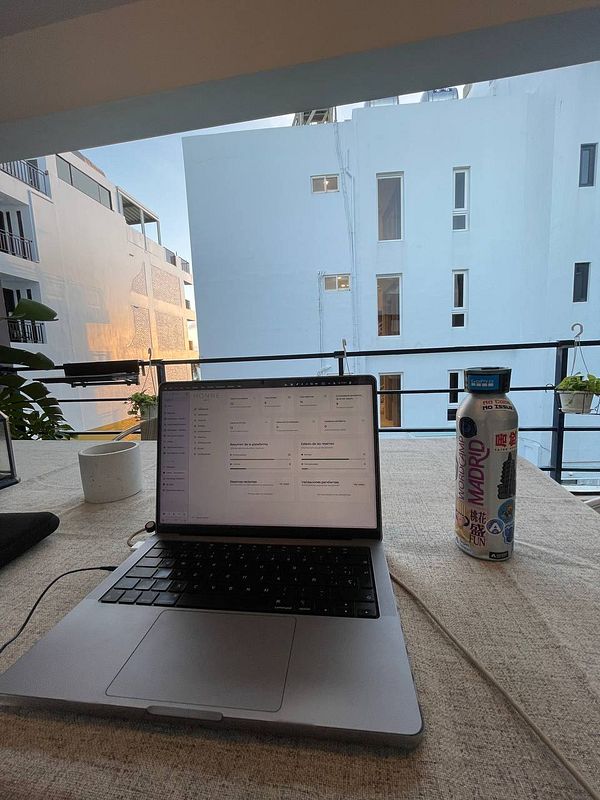 A workspace setup featuring a laptop, a drink, and a view of a building.