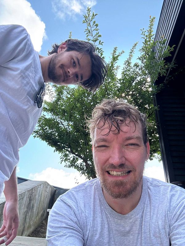 Two men are taking a selfie outdoors, smiling and enjoying their time together.