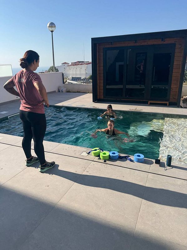 A personal trainer supervises two individuals exercising in a pool.