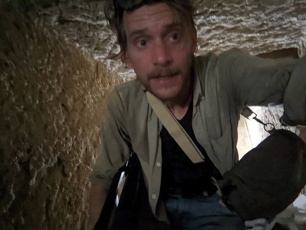 A person is navigating through a narrow, rocky passageway inside a pyramid.