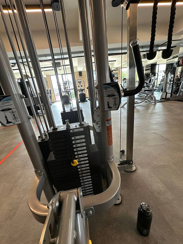A gym cable machine with visible weight stacks and workout area.