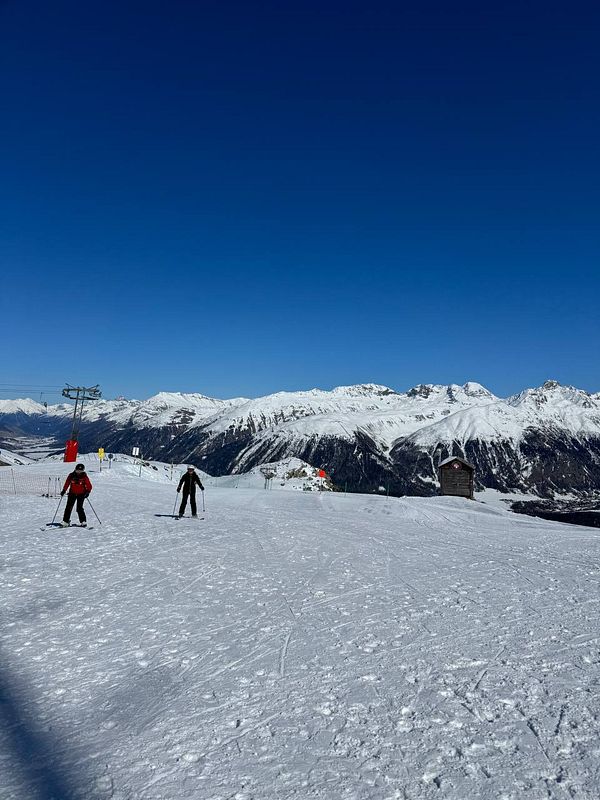 Two skiers navigate a snowy slope under a clear blue sky.