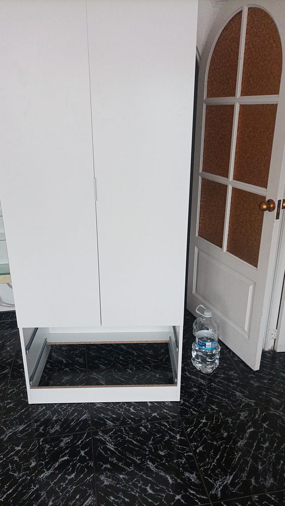 Assembled corner TV stand with glass shelves in a living room next to a window with floral curtains.