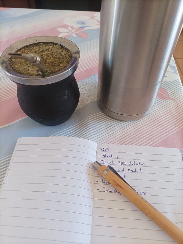 A workspace setup featuring a traditional mate drink, a thermos, and a notebook with a to-do list.