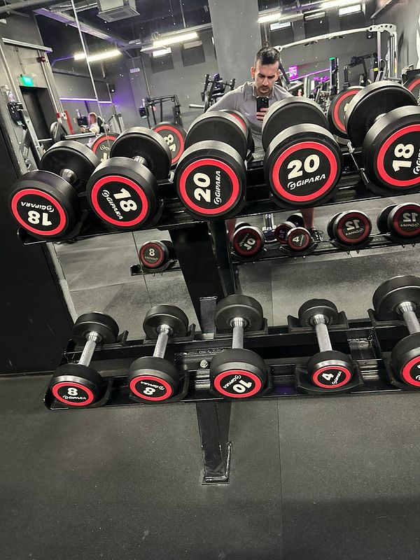 A gym setting featuring a rack of dumbbells with a person taking a selfie in the mirror.