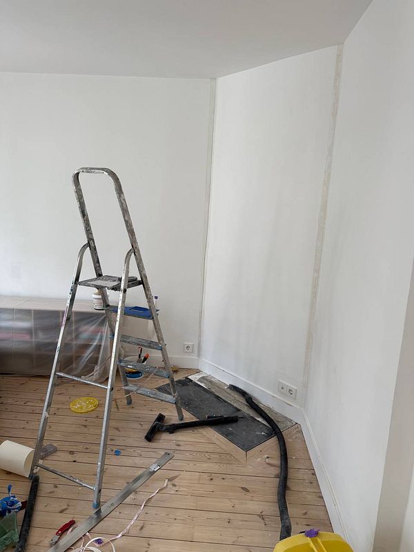 A partially renovated room with a ladder and tools for finishing touches on a wall.