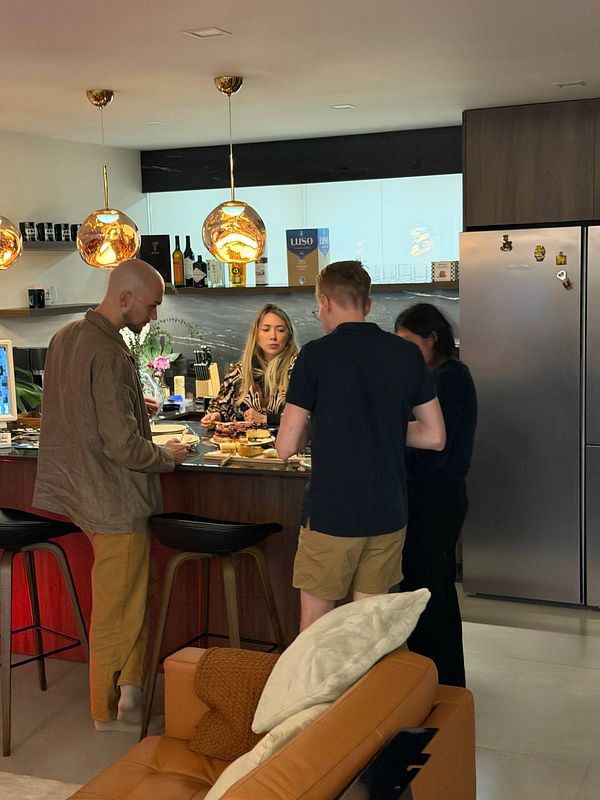 Four people gathered around a kitchen island enjoying food and drinks in a modern home kitchen setup.