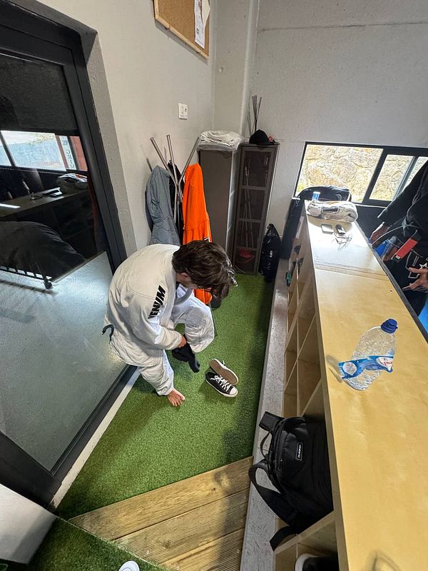 A person is preparing for Brazilian Jiu-Jitsu by putting on their shoes in a training facility.