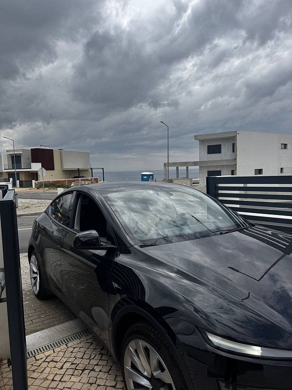 A black car is parked in front of modern buildings under a cloudy sky.