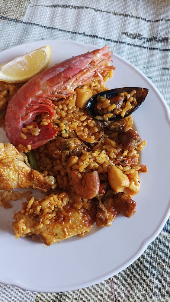 A plate of paella featuring seafood and chicken, garnished with a lemon wedge.