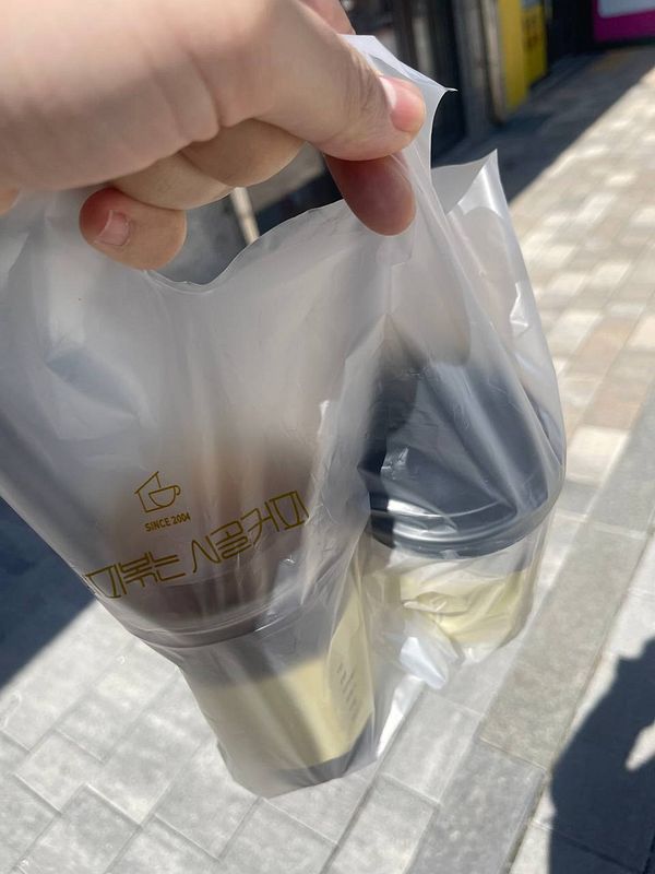 A hand holds a bag containing two takeaway coffee cups.
