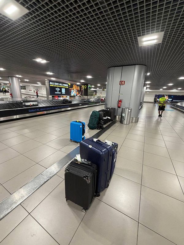 An empty luggage belt area at Lisbon Airport with several suitcases placed off to the side and a person walking away.