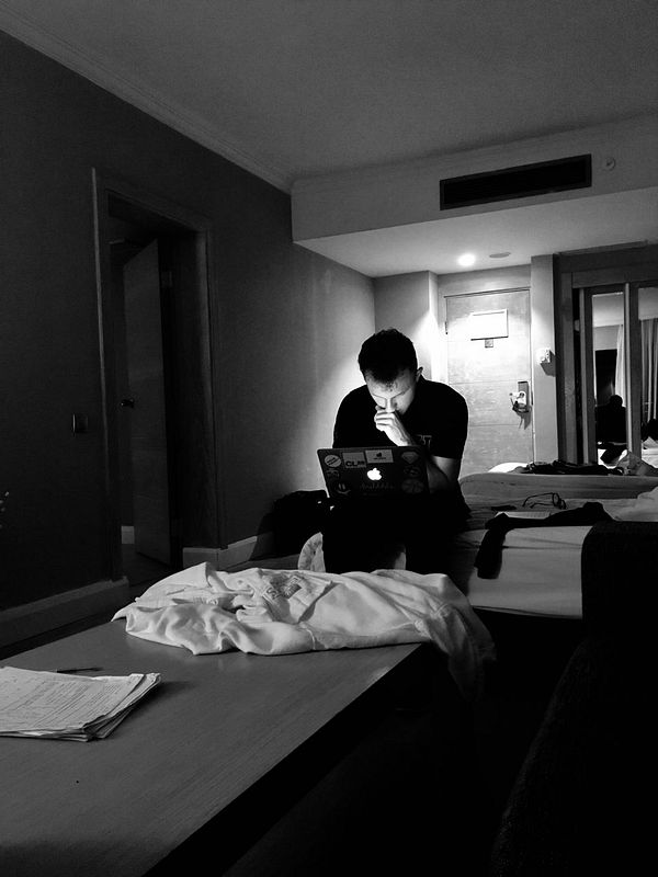 A person is focused on a laptop in a dimly lit hotel room.