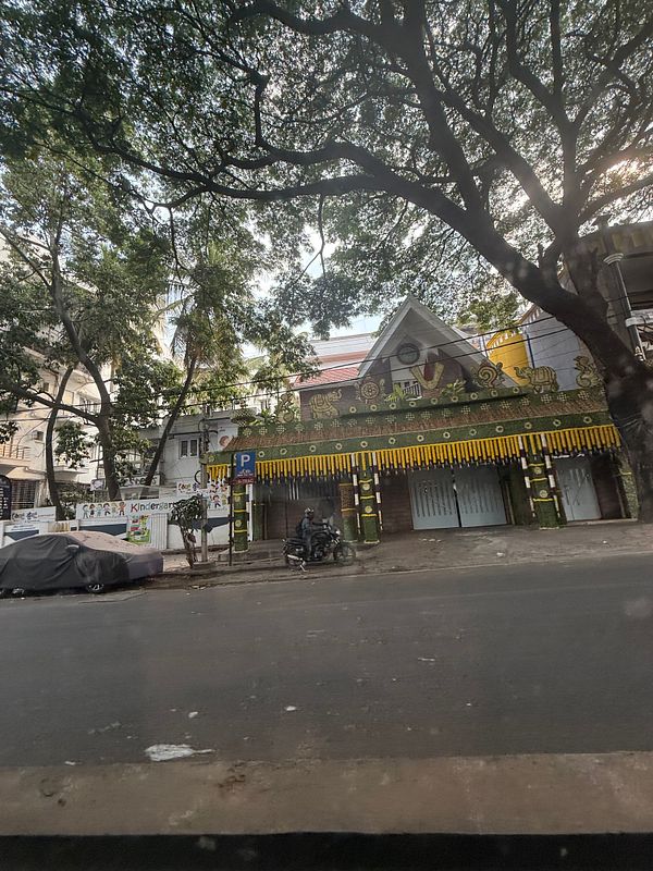 A colorful pavilion in Bangalore is surrounded by lush trees and parked vehicles.