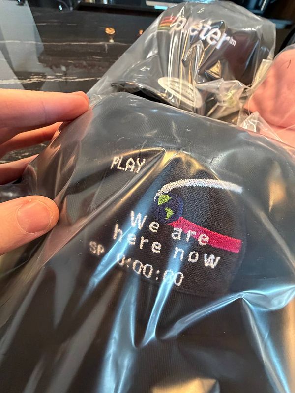 The image features a close-up of a packaged item of merchandise with embroidered text and graphics.