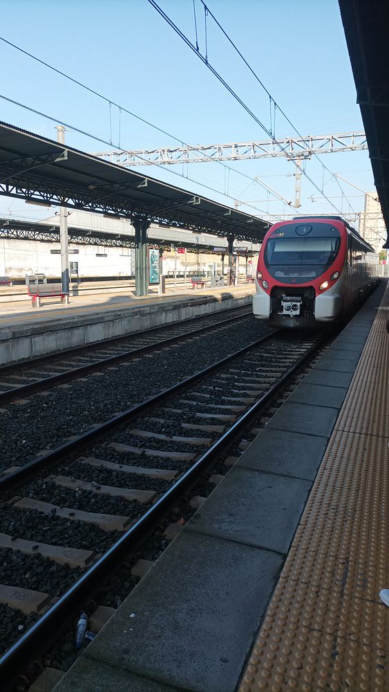 A train is stationed at a railway platform under a clear blue sky.