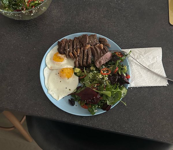 A plate of breakfast featuring eggs, sliced steak, and a fresh salad.