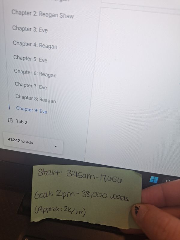 A hand holding a sticky note with writing, alongside a computer screen displaying a word count and chapter list.