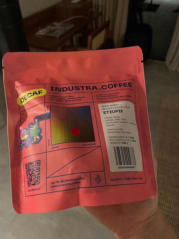 A hand holds a pink package of decaffeinated coffee labeled 'INDUSTRA.COFFEE'.