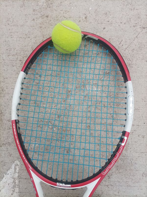 A tennis racket with a bright yellow tennis ball resting on its strings.