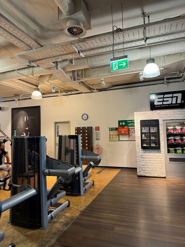 The image depicts the interior of a gym featuring workout equipment and various informational displays.