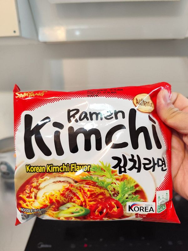 A hand holds a package of Korean kimchi ramen.