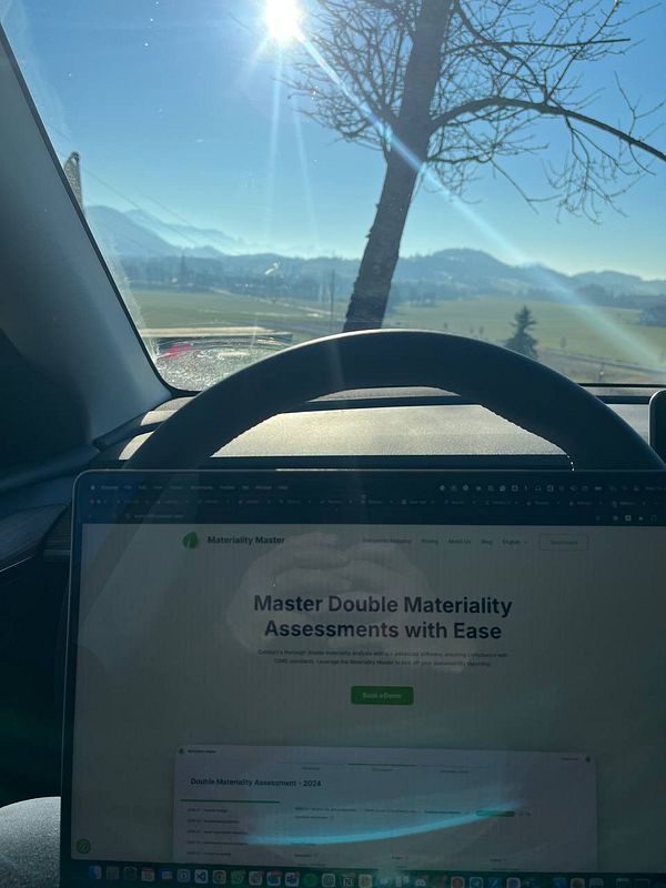 A laptop displaying a webpage is positioned inside a car, with a scenic view of mountains and a bright sun in the background.