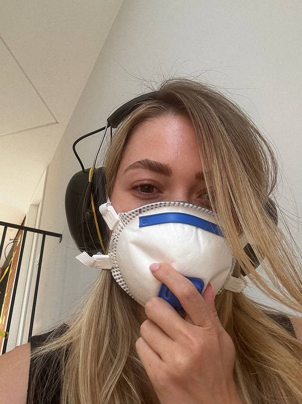 A woman wearing a protective mask and headphones is in a dusty environment.