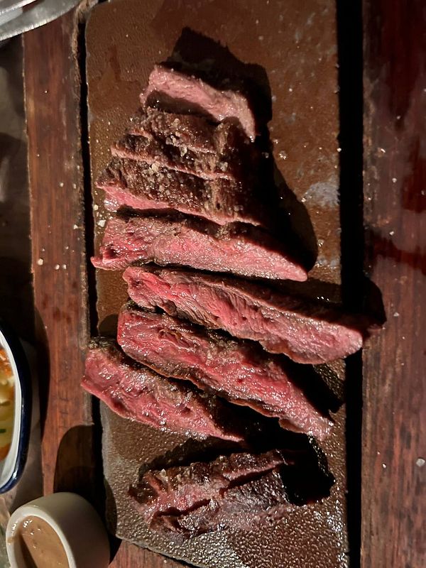 Close-up of a medium-rare grilled steak on a white plate with a green garnish and a fork.